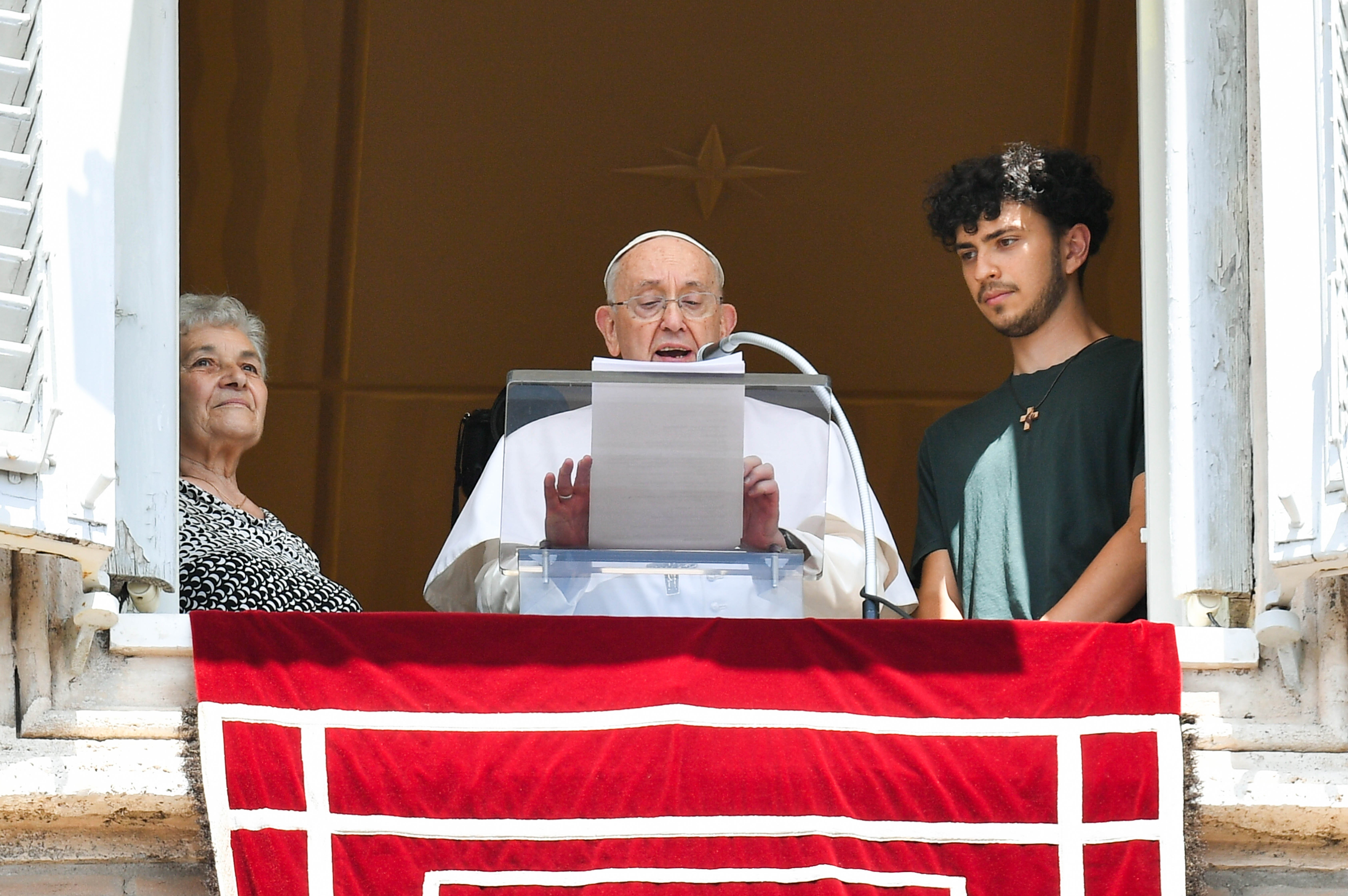 Pope Francis speaks from window alongside a young person and an elderly person. 