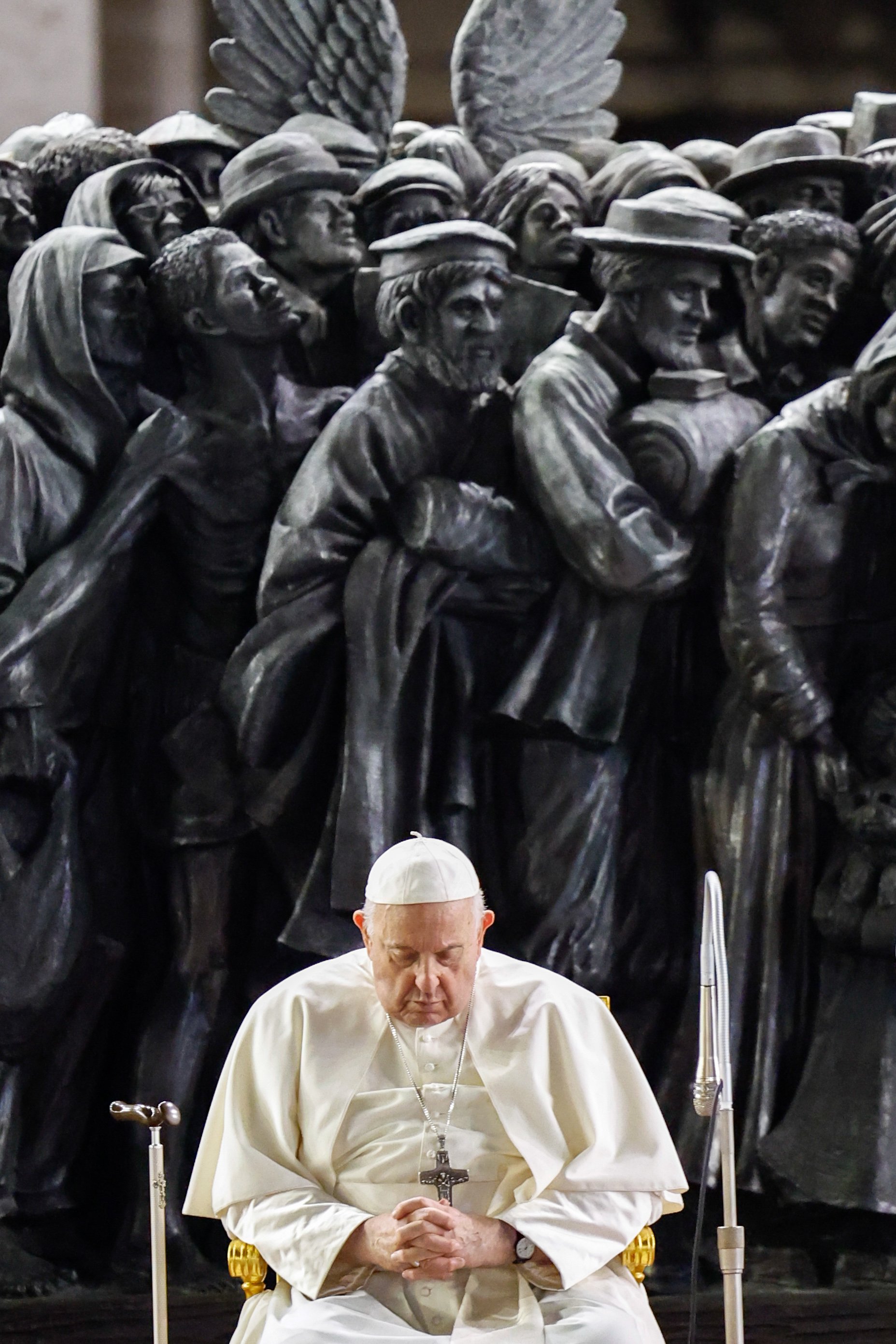 Pope Francis prays before a statue of migrants.