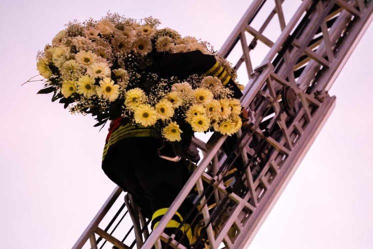 A firefighter carries flowers up a ladder.